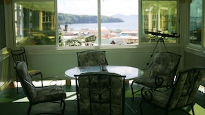 A sunroom with a view of a lake and mountains, featuring a round table and four chairs with floral upholstery. - Fairview Guest House (Kingstown)