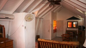 A room with a ceiling fan, a white air conditioner, a wooden bench, a small table, and a television. - Fairview Guest House (Kingstown)