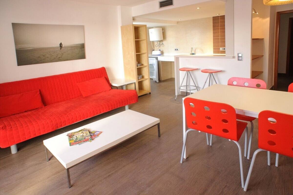 Un salon moderne avec un canapé rouge, une table basse blanche et un coin repas avec des chaises rouges.