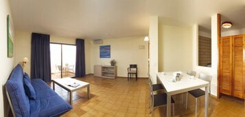 Una sala de estar con sofá, una mesa de comedor con sillas, una pequeña zona de cocina y un armario con puerta corredera.