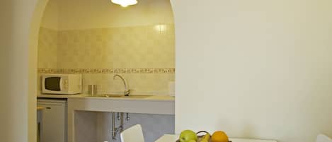 Cocina compacta con microondas, lavamanos y una cesta de fruta sobre la mesa.