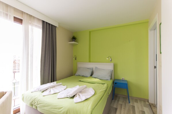 A neatly made bed with towels, a bedside table, and a small shelf with a plant.