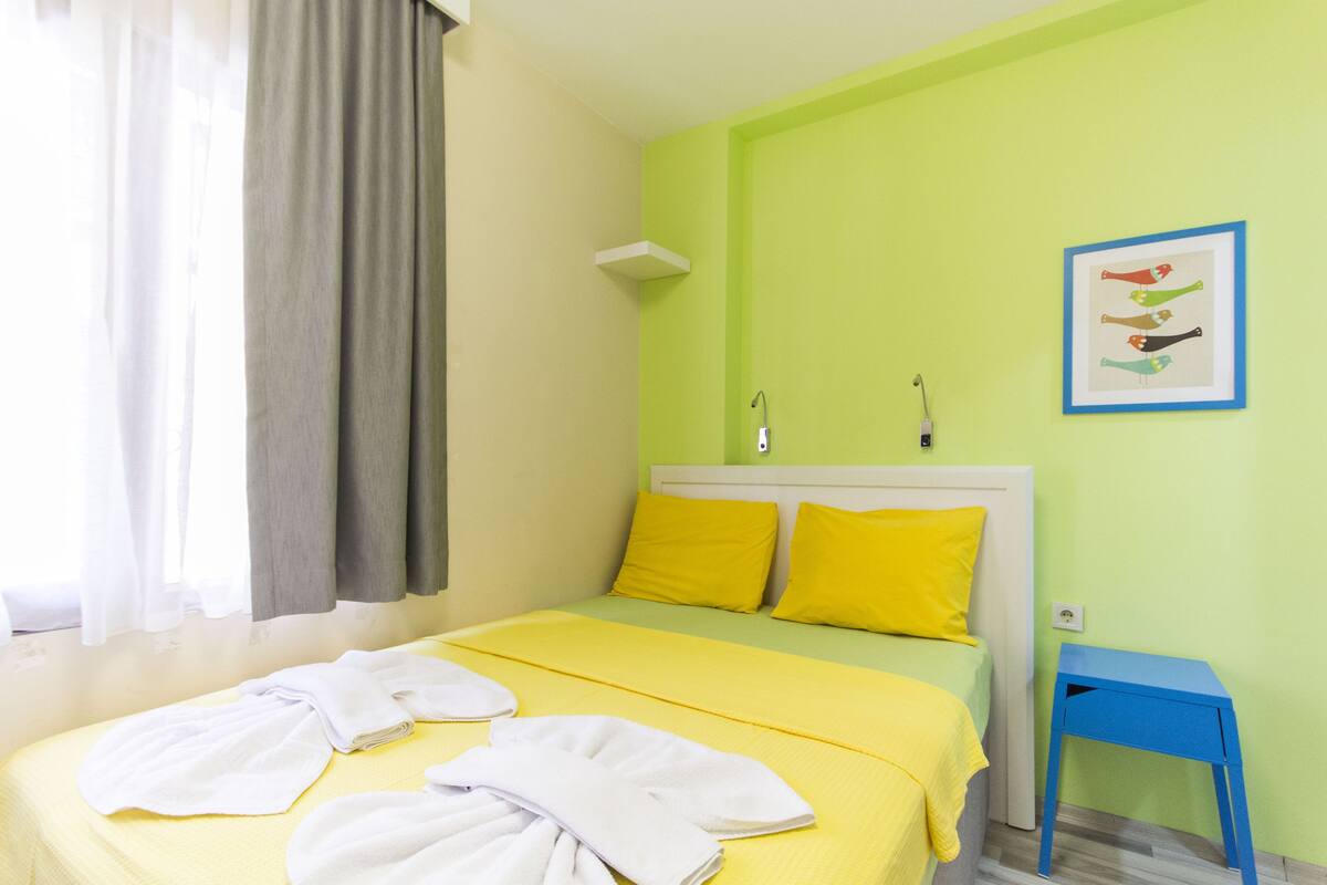 A hotel room with a bed, yellow bedding, a blue nightstand, and a framed picture on the wall.
