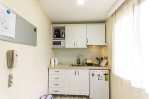 A compact kitchen with white cabinets, a microwave, a coffee maker, and a dishwasher. There is a bulletin board with papers and a telephone on the wall.