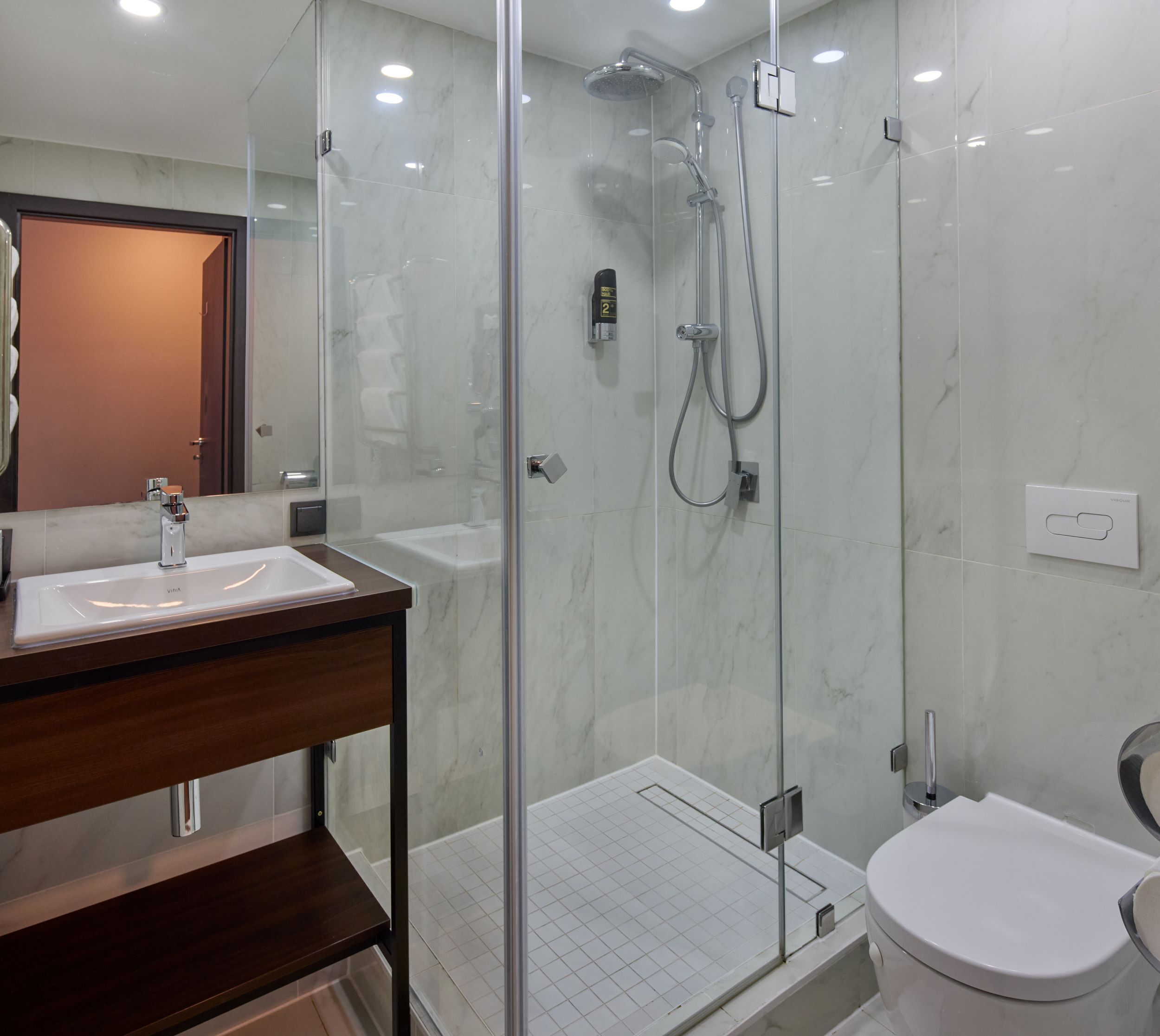 Ein modernes Badezimmer mit einer Duschkabine aus Glas, einem Holzbadezimmermöbel und einer weißen Toilette.