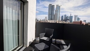 Un balcón con mobiliario de mimbre, puerta de cristal y vista al horizonte urbano.