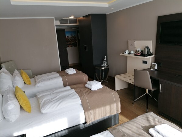 Habitación de hotel con una cama grande, un escritorio, una silla, un televisor y una mesita con una tetera.