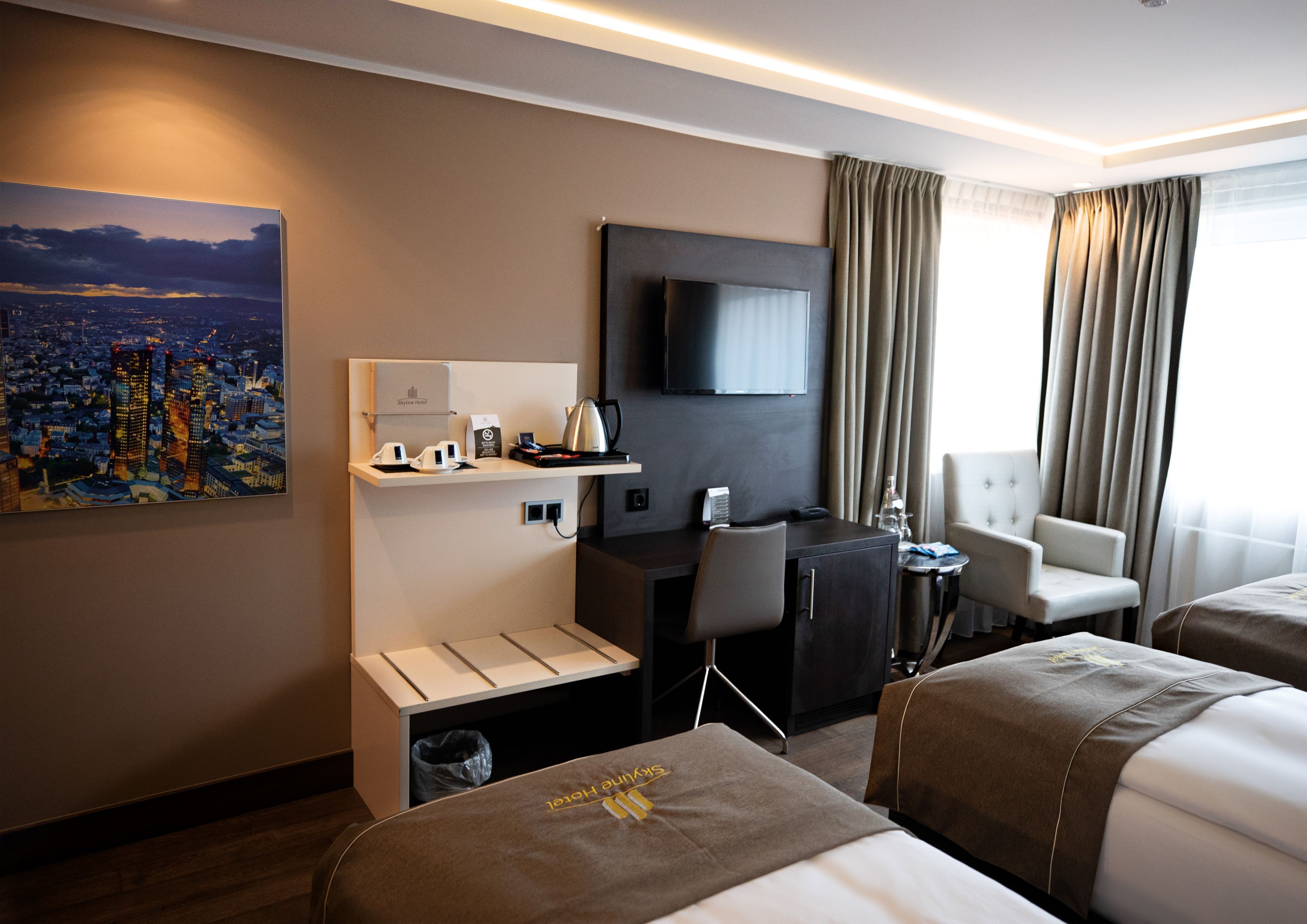 A hotel room with a bed, a desk, a chair, a TV, and a painting of a cityscape.