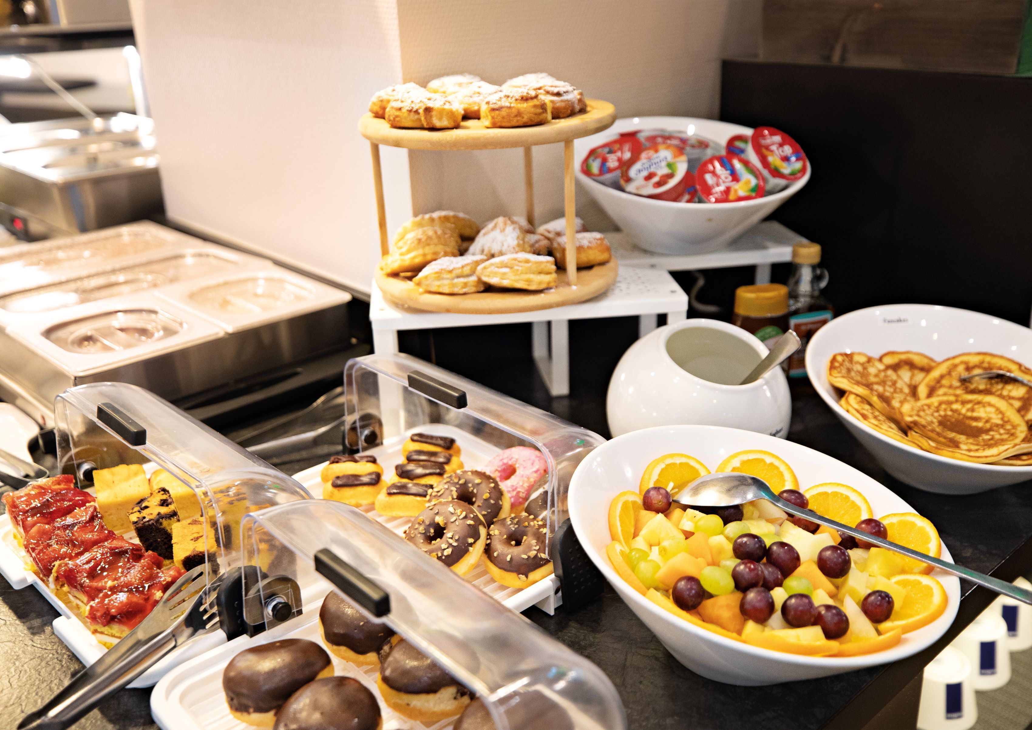 A buffet with various food items including pastries, fruits, and a bowl of yogurt.