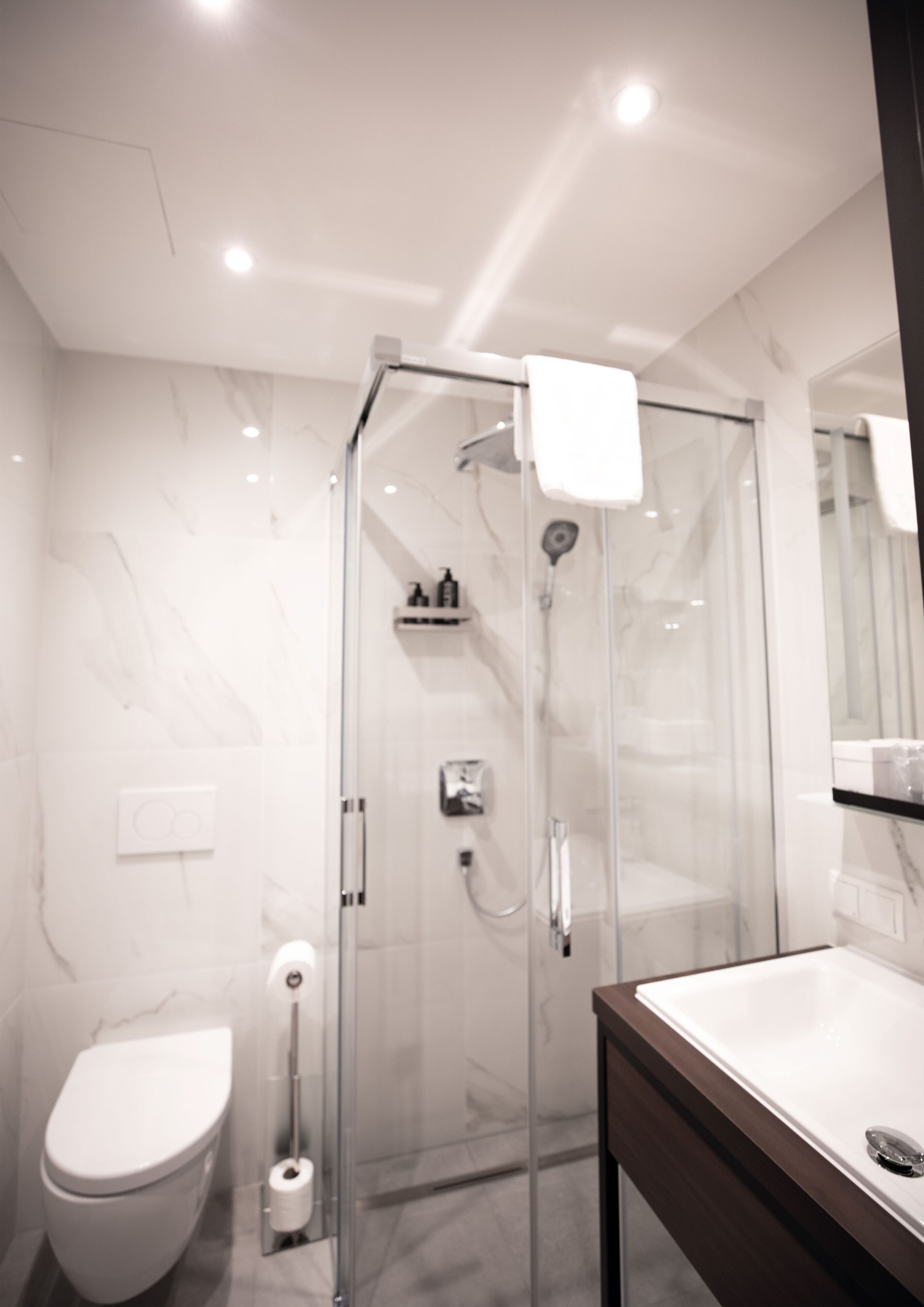 Ein modernes Badezimmer mit einer gläsernen Duschkabine, einer weißen Toilette und einer Wand mit Marmorfliesen.