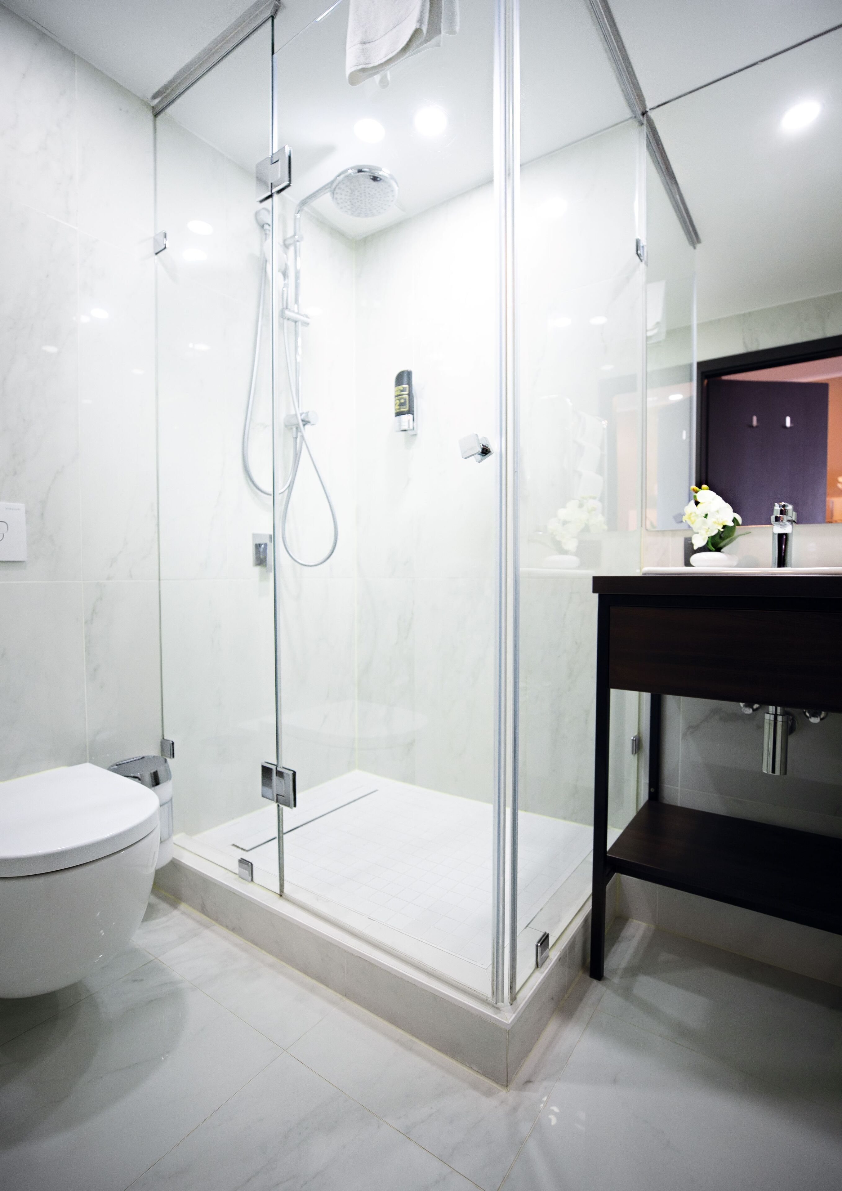 A modern bathroom with a glass-enclosed shower, a white toilet, and a dark wooden vanity with a mirror.