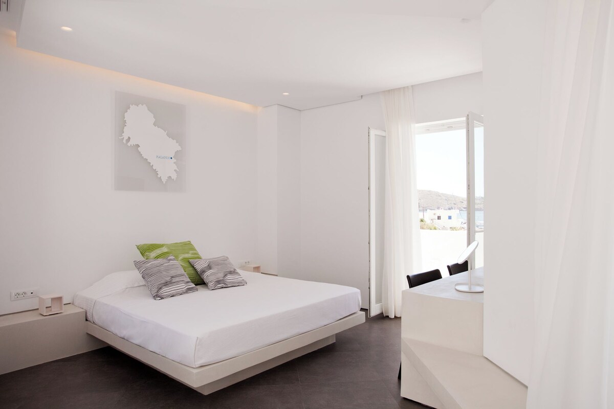 Un dormitorio moderno con cama, escritorio y vista al mar.