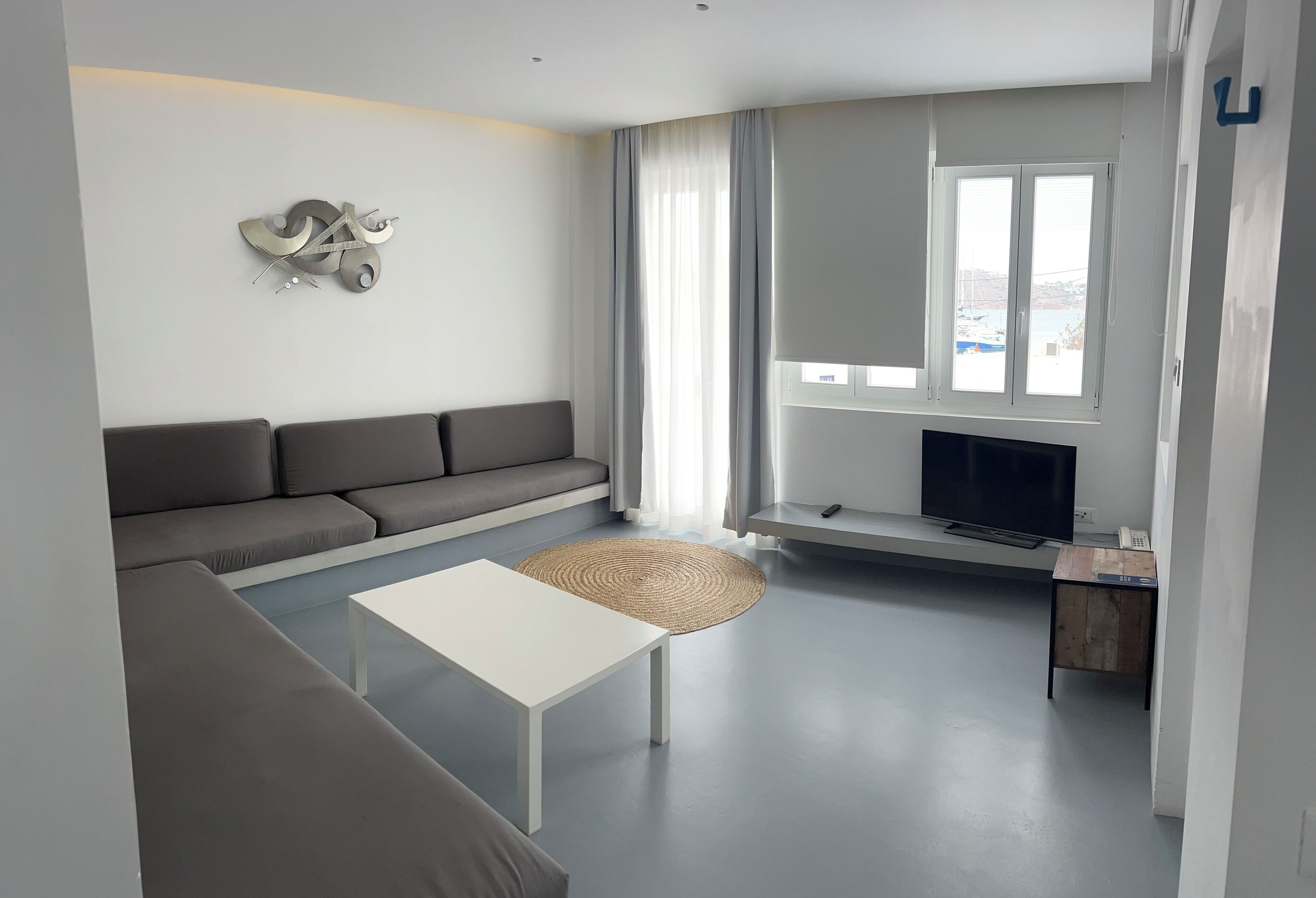 A modern living room with a grey sofa, a white coffee table, and a flat-screen TV on a stand.