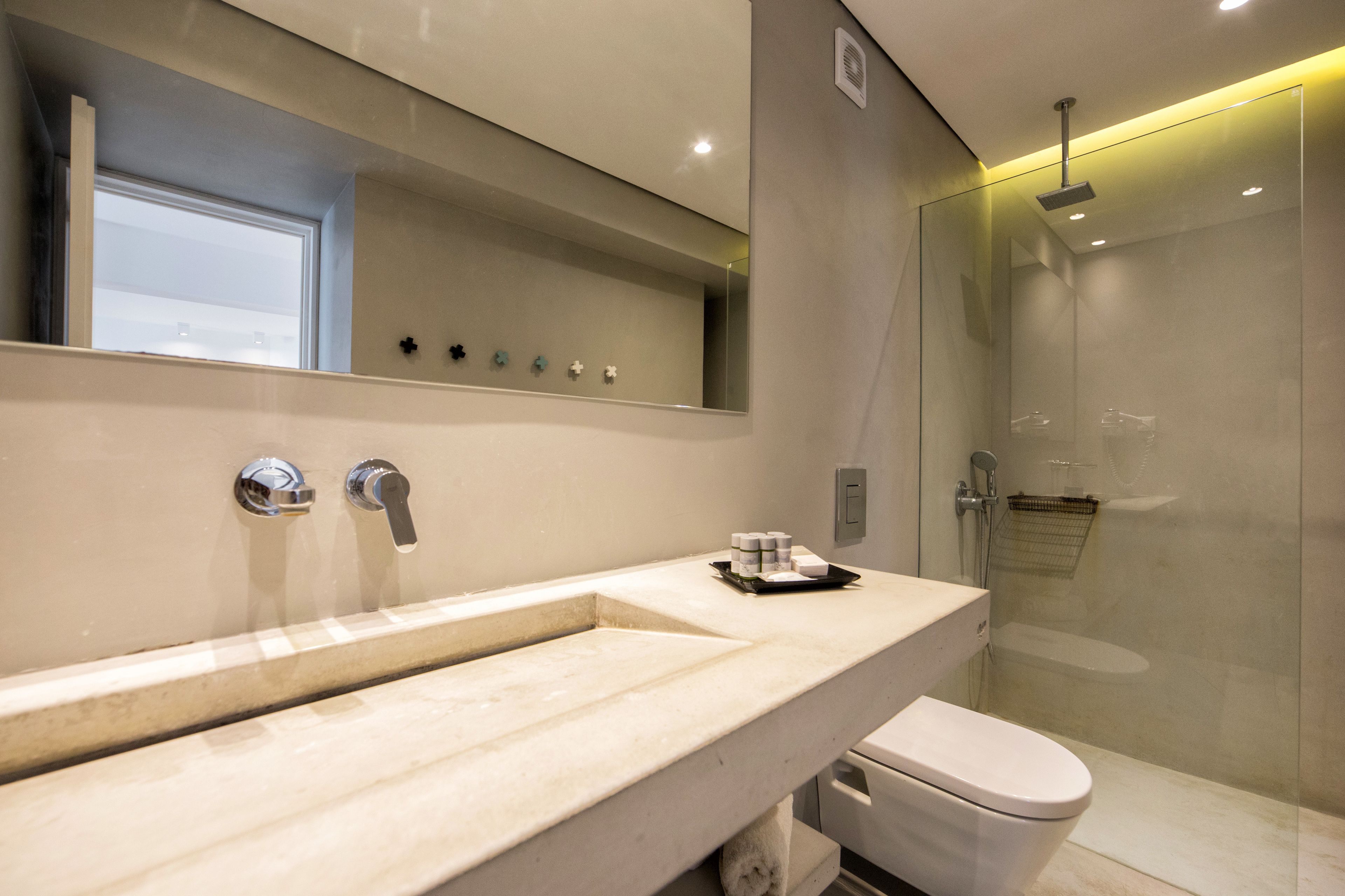 A modern bathroom with a large mirror, a marble sink, a toilet, and a glass-enclosed shower.