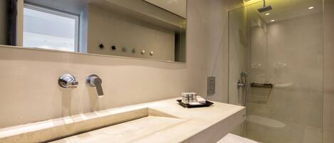 A modern bathroom with a large mirror, a marble sink, a toilet, and a glass-enclosed shower.