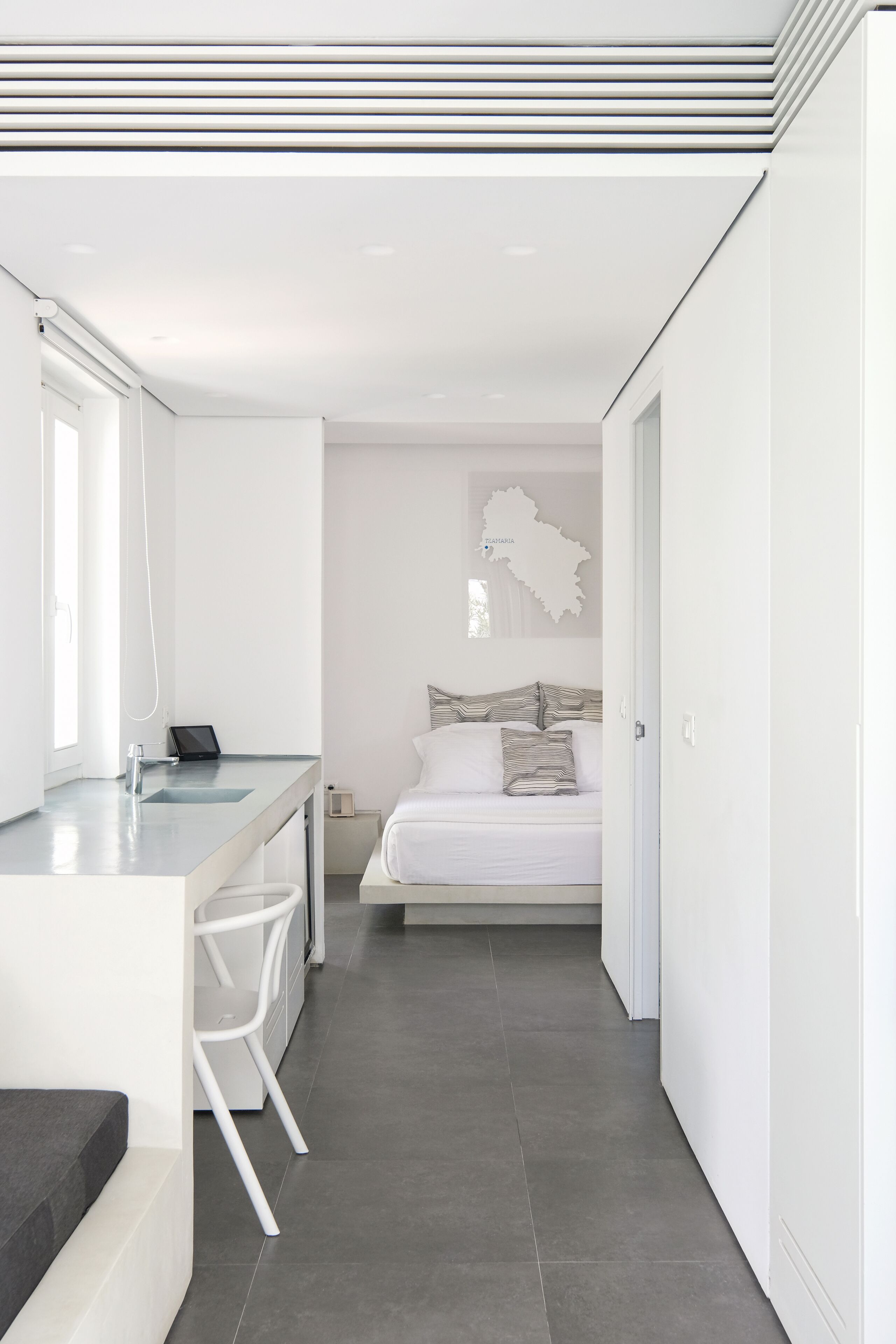 Une chambre à coucher moderne et minimaliste, dotée d’un grand lit, d’une table de chevet et d’un bureau intégré avec une chaise.