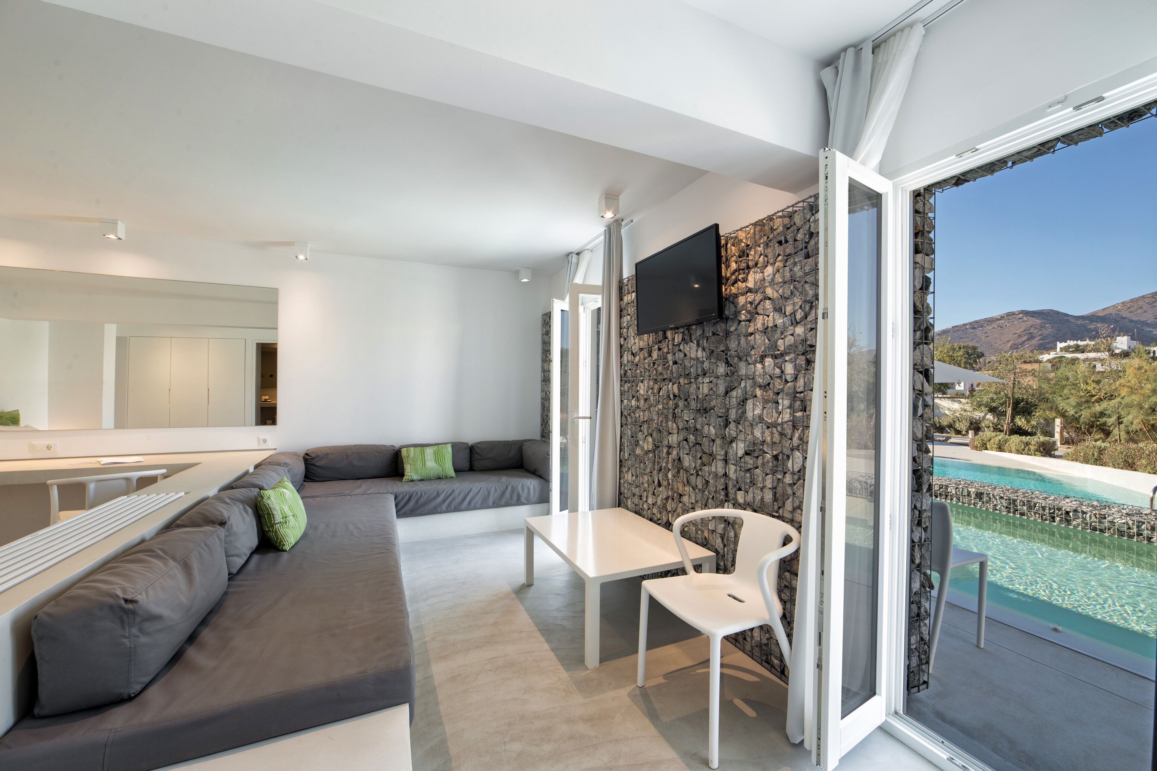 A modern living room with a sofa, a dining table, and a TV mounted on a stone wall.