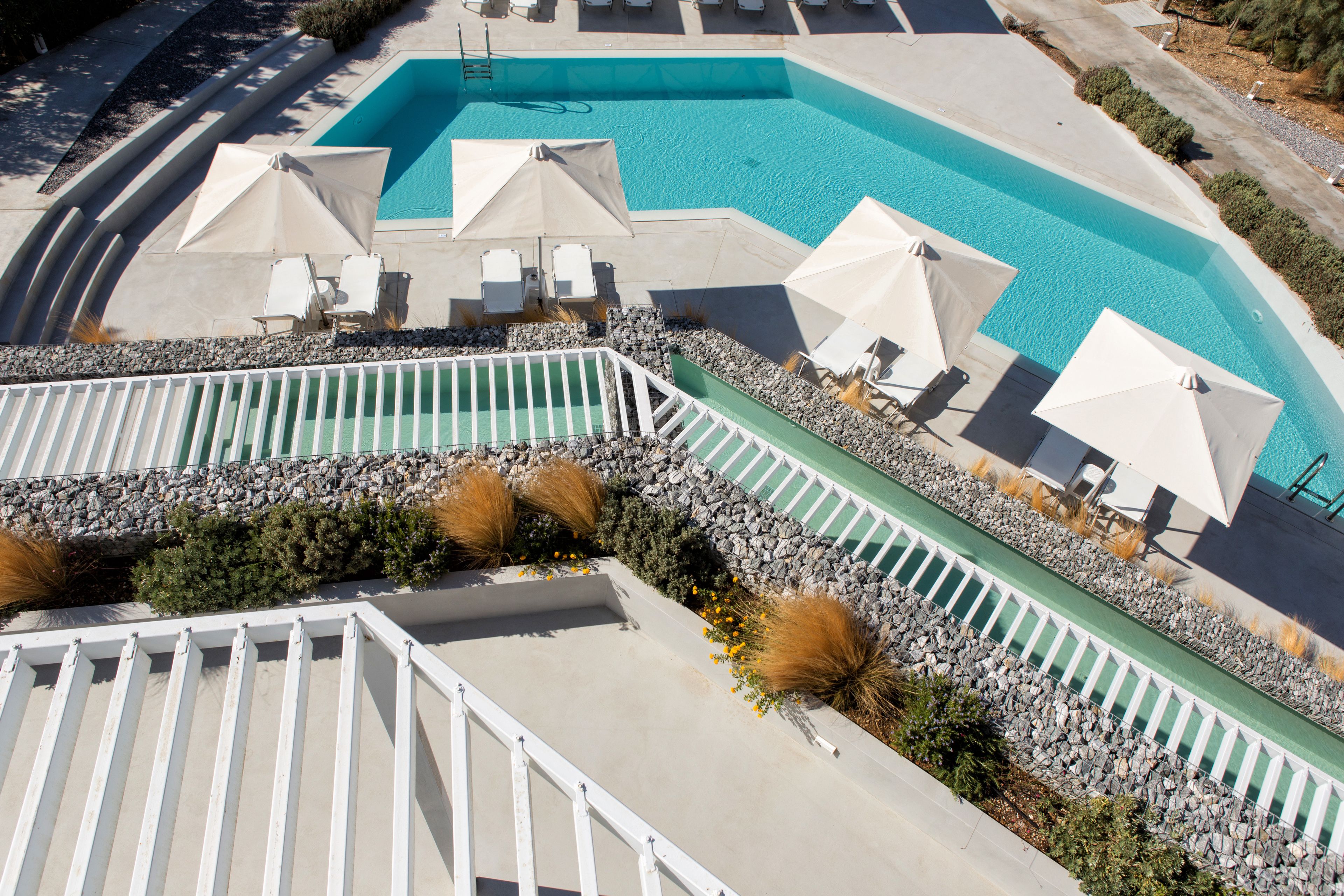 A swimming pool with lounge chairs and umbrellas, surrounded by a stone wall and greenery.