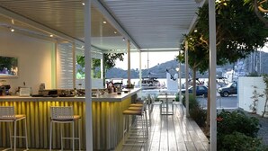Zona de bar con mostrador, taburetes y vista al puerto con barcos y coches.