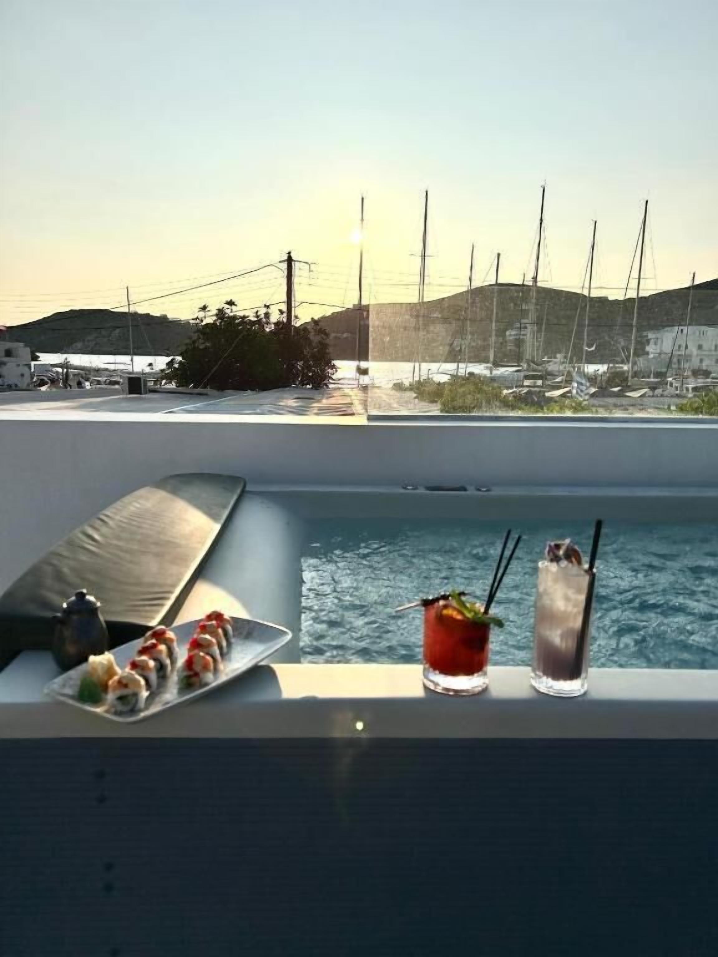 A poolside area with a sushi platter, two drinks, and a teapot.