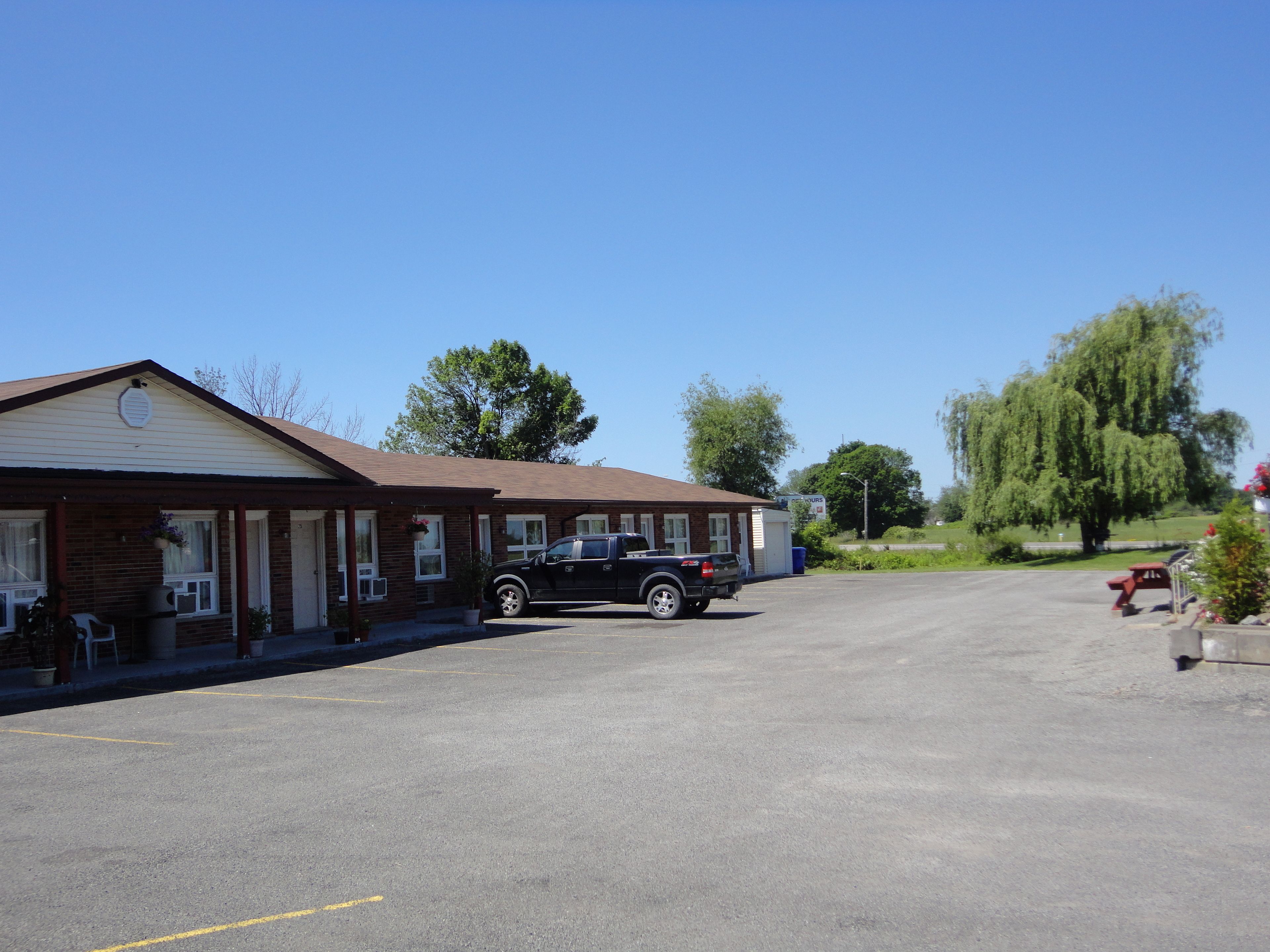 Un motel con una camioneta estacionada, una zona de estacionamiento techada y un pequeño edificio con porche.