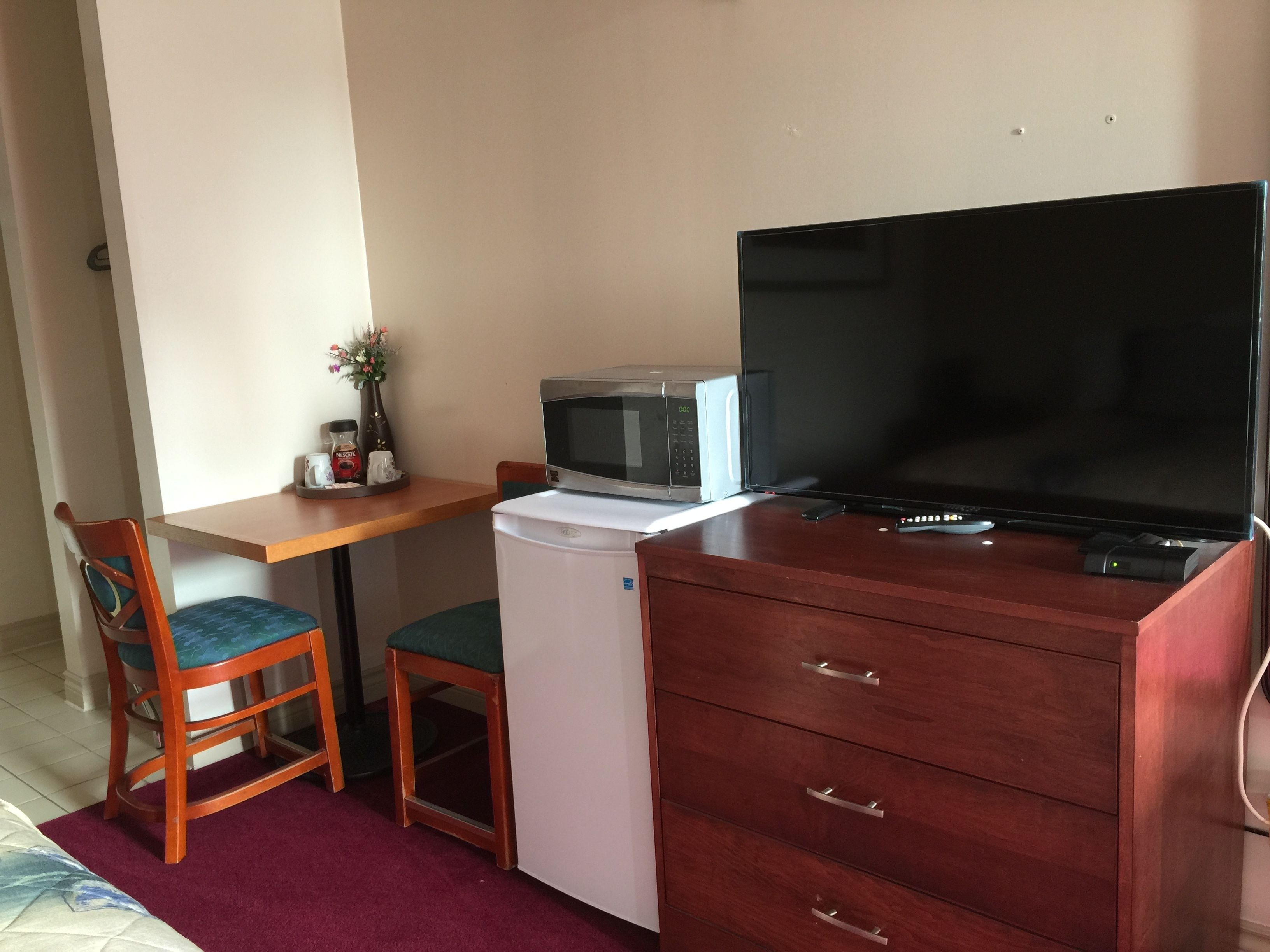 Una kitchenette compacta con microondas, un refrigerador pequeño, una silla de madera y un televisor sobre un mueble de madera.