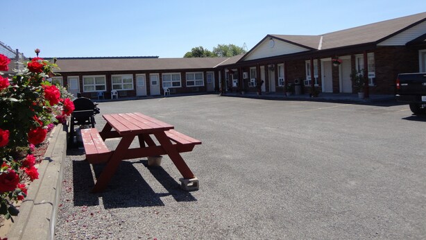 A motel with a parking lot, a picnic table, and a row of rooms with windows and air conditioning units. - Good Night Inn (Port Colborne)