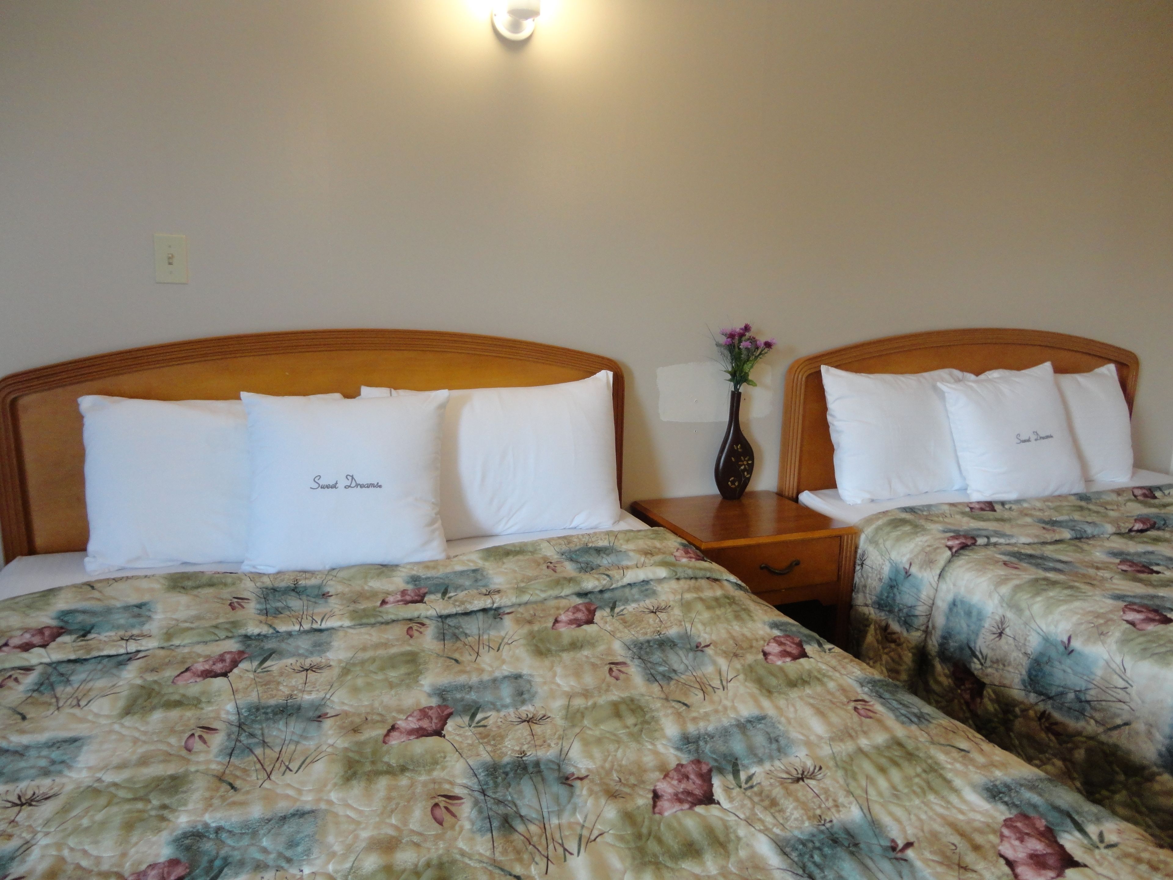 Dos camas dobles con ropa de cama estampada, una mesita de noche con un florero y una lámpara de pared.