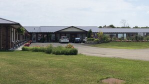 A building with a brick facade, a covered entrance, and a parking area with cars. - Good Night Inn (Port Colborne)