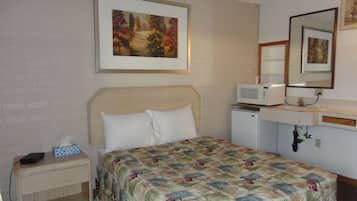 Hotelkamer met een bed, nachtkastje, magnetron, wastafel en spiegel.