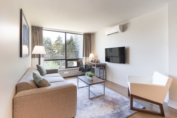 A modern living room with a sofa, a chair, a coffee table, and a TV. - Gage Suites at UBC (Vancouver)
