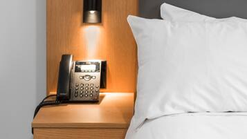 A hotel room with a wooden nightstand, a telephone, and a bed with white bedding.