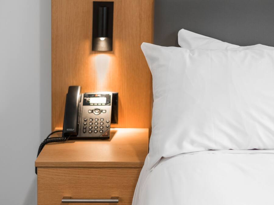 A hotel room with a wooden nightstand, a telephone, and a bed with white bedding.