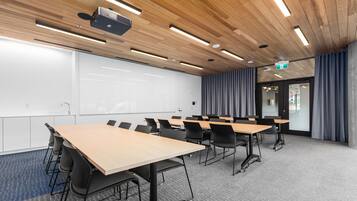 Une salle de conférence équipée de plusieurs tables et chaises, d’un tableau blanc et d’un projecteur fixé au plafond.