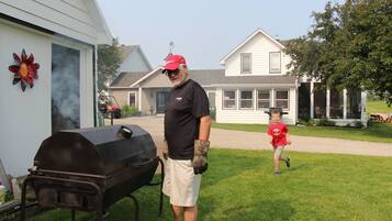 A man standing next to a barbecue grill in a backyard with a house in the background.