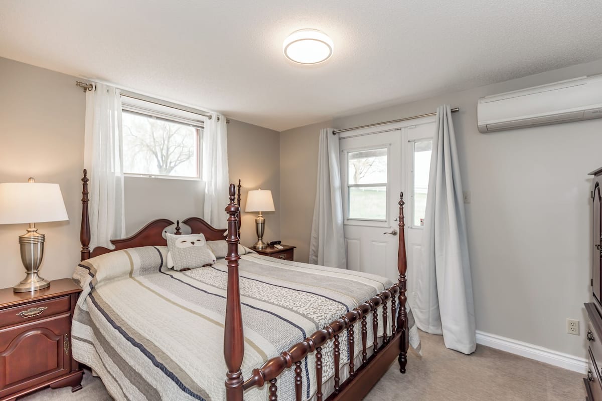Une chambre à coucher avec un lit à baldaquin, deux tables de chevet avec des lampes, une commode et une fenêtre avec des rideaux.