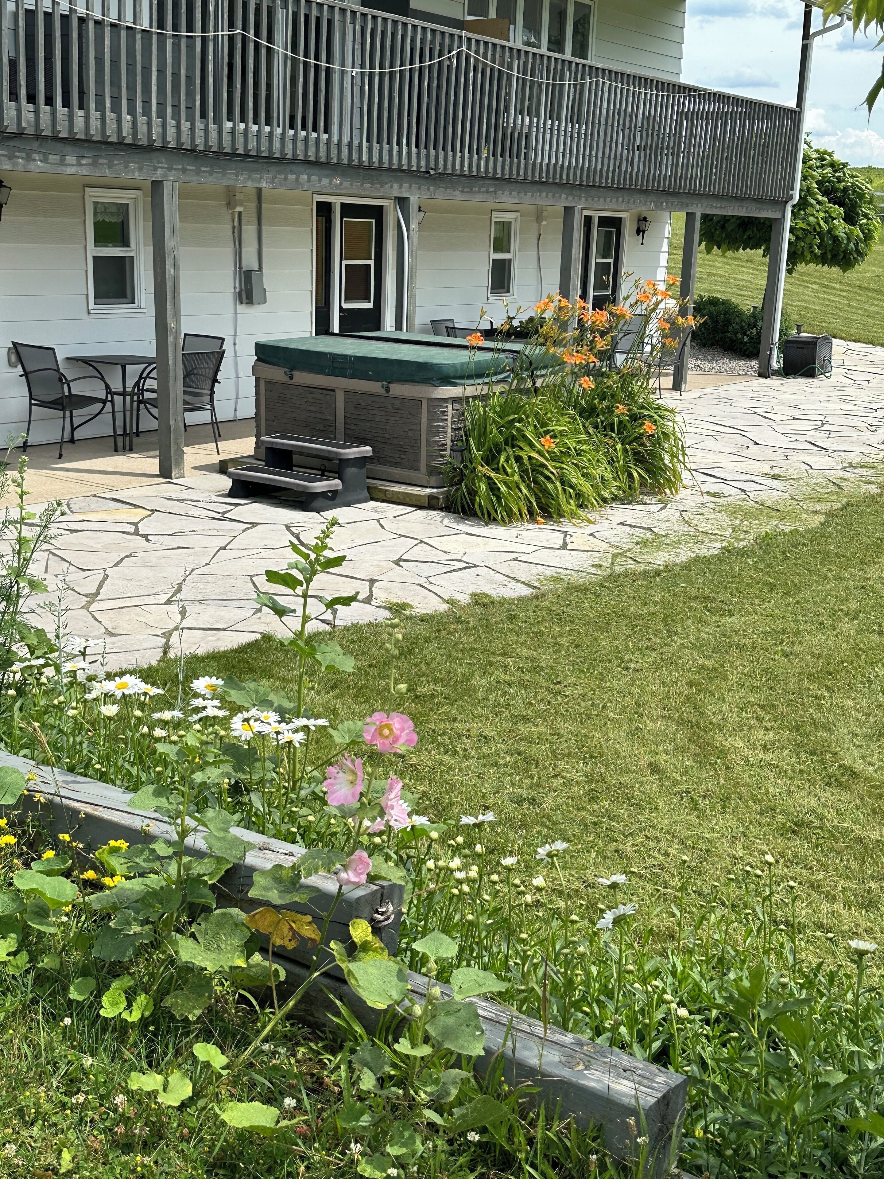 A house with a patio area featuring a hot tub, outdoor seating, and a garden with flowers.