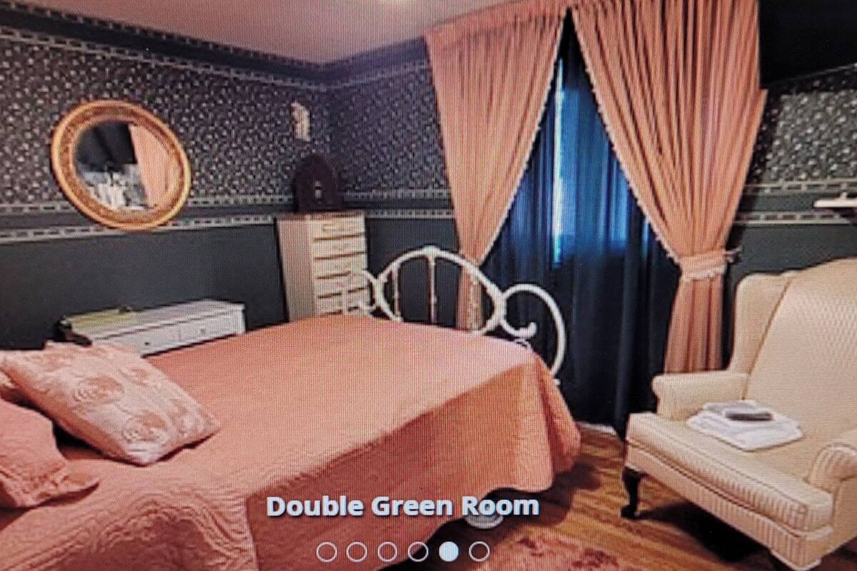 Quarto duplo com decoração verde, uma cama, uma poltrona, uma cômoda e um espelho.