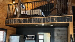 A rustic cabin interior with a loft bedroom, a kitchen area, and a bathroom. - Hideout on the Horseshoe (New Braunfels)