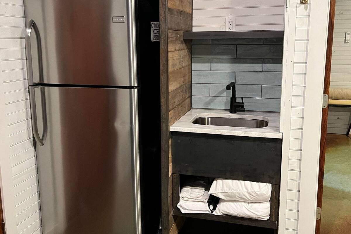 Eine kompakte Küche mit einem Edelstahl-Kühlschrank, einer Spüle und einer Holz-Spritzschutzwand.