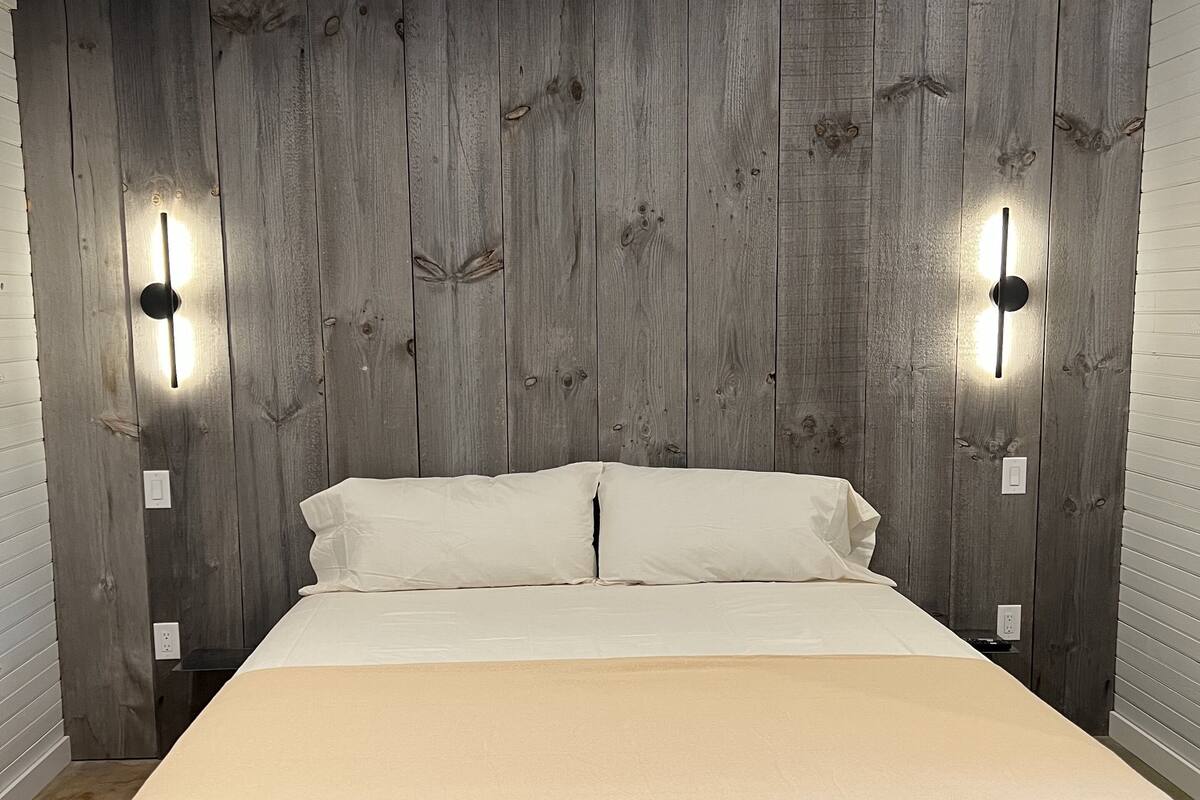 Ein Schlafzimmer mit einem Holzkopfteil, einem Bett mit weißen Bettwäsche und zwei Wandleuchten.