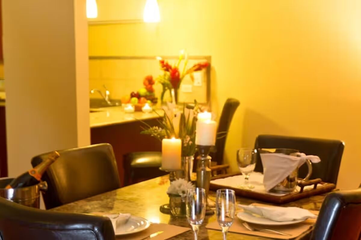 Une table à manger, avec des chaises, des bougies et un vase de fleurs.