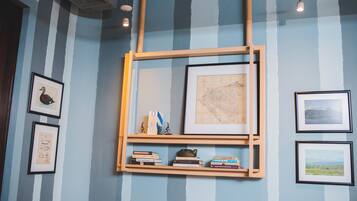 A room with striped walls, a wooden shelf with books and framed items, and a framed map on the wall.