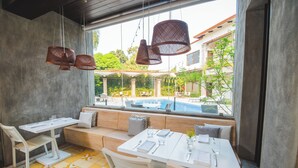 Un coin repas avec une table dressée pour deux personnes, un banc et des lampes en osier suspendues.