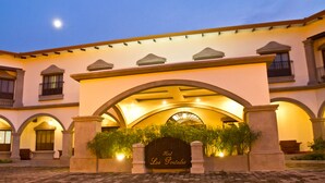 L’entrée d’un hôtel, avec une façade en arc de cercle, une enseigne indiquant « Los Portales » et un chemin pavé.