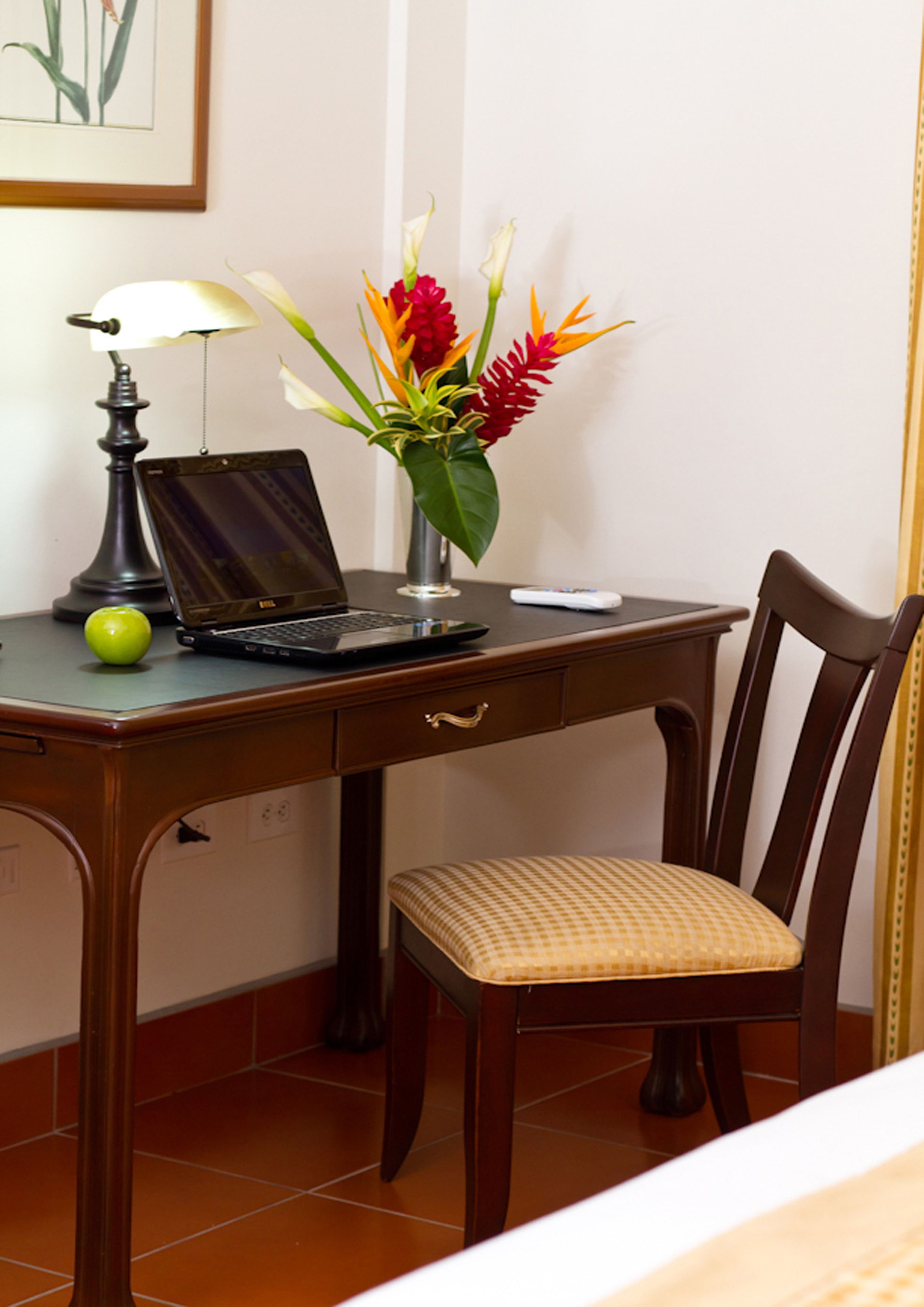 Un bureau en bois avec un ordinateur portable, une lampe et un vase de fleurs.
