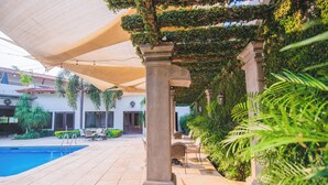 Un espace aménagé au bord de la piscine, doté d’une pergola, de sièges et d’une végétation luxuriante.