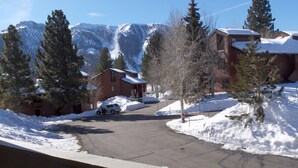 A residential street with snow-covered houses, a parked car, and a mountain backdrop.