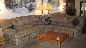 A living room with a sectional sofa, a wooden coffee table, and a large wall mural of a forest scene.