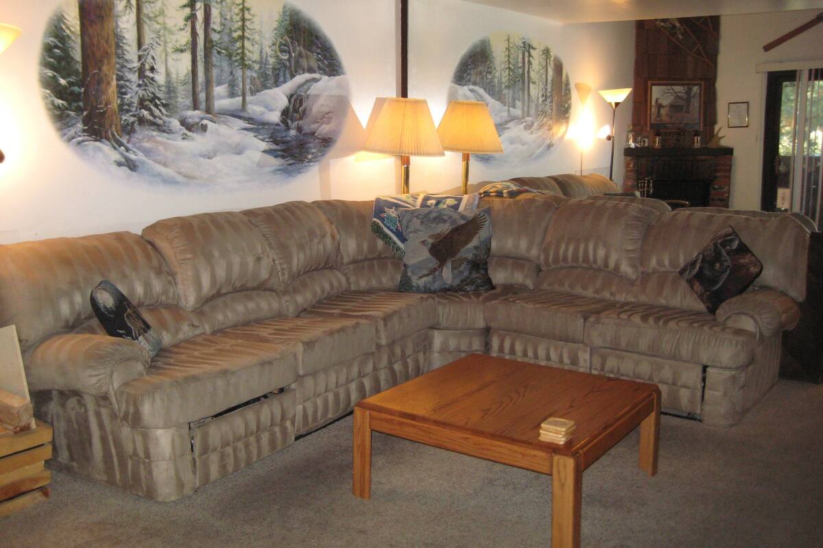 A living room with a sectional sofa, a wooden coffee table, and a large wall mural of a forest scene.